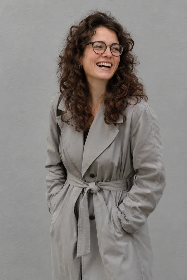 Mujer sonriente con gabardina gris de algodón anudada a la cintura, sobre fondo gris